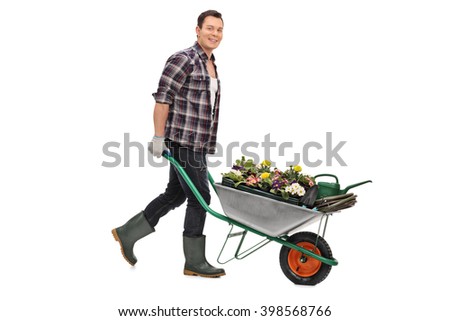 Young gardener pushing a wheelbarrow full of gardening equipment and flowers isolated on white background