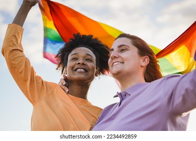 Young gay couple holding LGBT rainbow flag outdoor at pride parade - Powered by Shutterstock