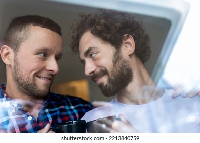 Young Gay Couple In Love Looking Out The Window. Two Young Androgynous Men Smiling Together And Having Coffee.