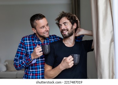 Young Gay Couple In Love Looking Out The Window. Two Young Androgynous Men Smiling Together And Having Coffee.