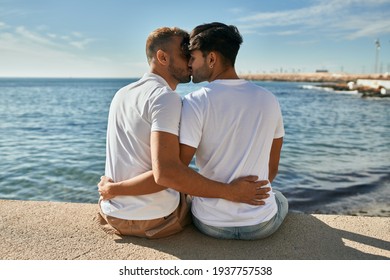 Young Gay Couple On Back View Kissing At The Beach Promenade.