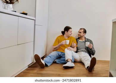 A young gay couple sits on the floor of their modern kitchen, enjoying a cup of coffee and each others company. - Powered by Shutterstock