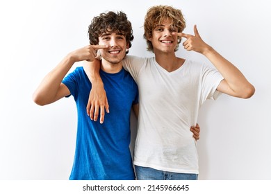 Young Gay Couple Standing Together Over Isolated Background Pointing With Hand Finger To Face And Nose, Smiling Cheerful. Beauty Concept 