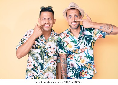 Young Gay Couple Of Two Men Wearing Summer Hat And Hawaiian Shirt Pointing With Hand Finger To Face And Nose, Smiling Cheerful. Beauty Concept 