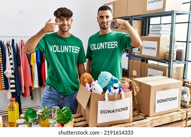 Young Gay Couple Wearing Volunteer T Shirt At Donations Stand Pointing With Hand Finger To Face And Nose, Smiling Cheerful. Beauty Concept 