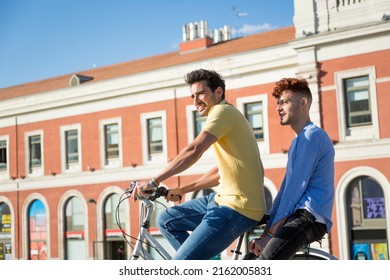 Young Gay Male Couple With Gay Pride Wristbands Enjoying A Bike Ride Outdoors. Lgbt Concept