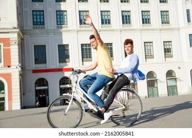 Young Gay Male Couple With Gay Pride Bracelets Having Fun Riding Bikes Outdoors. Lgbt Concept