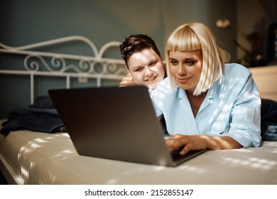 Young Gay Women Surfing The Net On Laptop While Relaxing In The Bedroom.