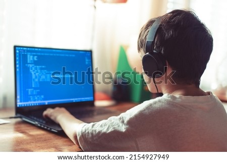 Young geek boy with headphones coding on laptop at home