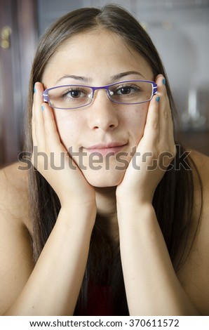 Young geeky girl with glasses and hands on a cheeks.
