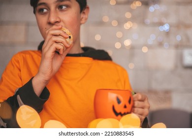 Young Generations Z Teen Boy In Orange Clothes While All Hallows Eve Photo Session At Home. Stylish Teenager With Cup Of Head Jack And Sweets Celebrates Halloween Holiday Enjoy Chocolate Candy