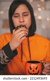 Young Generations Z Teen Boy In Orange Clothes While All Hallows Eve Photo Session At Home. Stylish Teenager With Cup Of Head Jack And Sweets Celebrates Halloween Holiday Enjoy Chocolate Candy