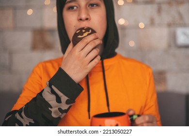 Young Generations Z Teen Boy In Orange Clothes While All Hallows Eve Photo Session At Home. Stylish Teenager With Cup Of Head Jack And Sweets Celebrates Halloween Holiday Enjoy Chocolate Candy