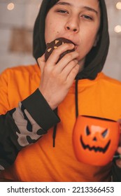 Young Generations Z Teen Boy In Orange Clothes While All Hallows Eve Photo Session At Home. Stylish Teenager With Cup Of Head Jack And Sweets Celebrates Halloween Holiday Enjoy Chocolate Candy