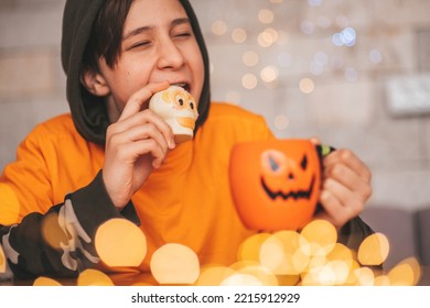 Young Generations Z Teen Boy In Orange Clothes While All Hallows Eve Photo Session At Home. Stylish Teenager With Cup Of Head Jack And Sweets Celebrates Halloween Holiday Enjoy Chocolate Candy