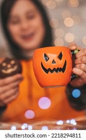 Young Generations Z Teen Boy In Orange Clothes While All Hallows Eve Photo Session At Home. Stylish Teenager With Cup Of Head Jack And Sweets Celebrates Halloween Holiday Enjoy Chocolate Candy