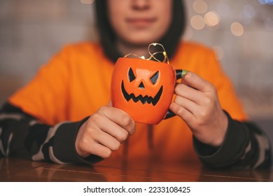 Young generations Z teen boy in orange clothes while all hallows eve photo session at home. Stylish teenager with cup of head Jack and sweets celebrates halloween holiday enjoy chocolate candy - Shutterstock ID 2233108425