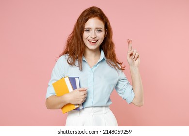 Young Ginger Student Woman In Blue Shirt Hold Book Wait Special Moment Keep Fingers Cross Making Wish Eyes Closed Isolated On Pastel Pink Background Education High School University College Concept