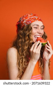 Young ginger woman in bandana laughing while eating water melon isolated over orange wall - Shutterstock ID 2071639322