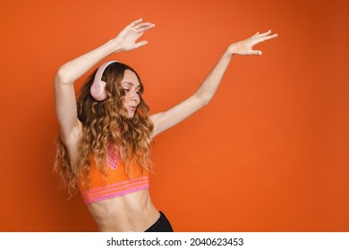 Young Ginger Woman Dancing While Listening Music With Headphones Isolated Over Orange Wall