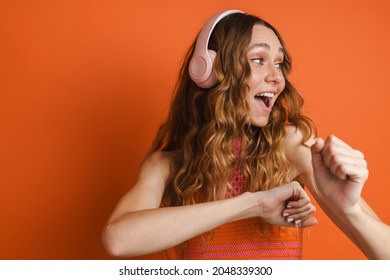 Young Ginger Woman Dancing While Listening Music With Headphones Isolated Over Orange Wall