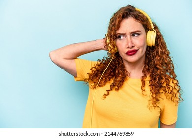 Young Ginger Woman Listening To Music Isolated On Blue Background Touching Back Of Head, Thinking And Making A Choice.