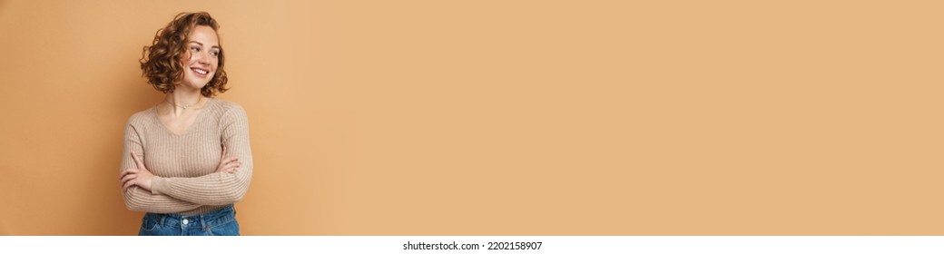 Young Ginger Woman Smiling While Posing With Arms Crossed Isolated Over Beige Background