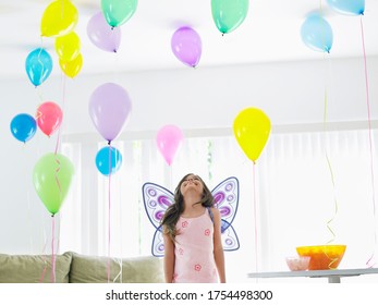 Young Girl (7-9) With Fairy Wings In Room Full Of Balloons