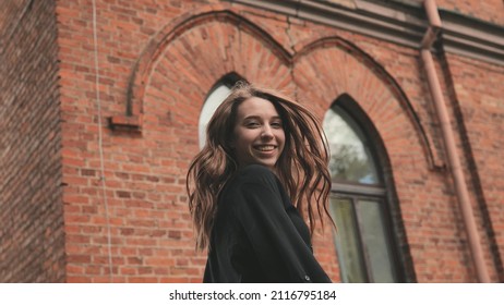 A young girl is actively posing against the backdrop of a brick building.