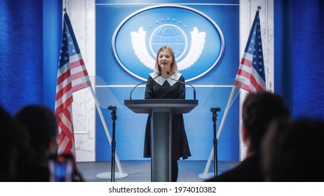 Young Girl Activist Greeting Visitors Before The Speech At Press Conference In Government Building. Child Speaking To Congress At Summit Meeting. Backdrop With United States Of America Flags.