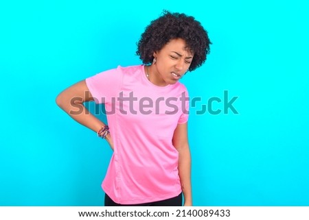 young girl with afro hair style wearing sport pink t-shirt over blue background Suffering of backache, touching back with hand, muscular pain