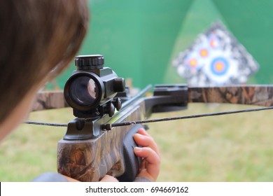 A young girl is aiming at a target from a crossbow.