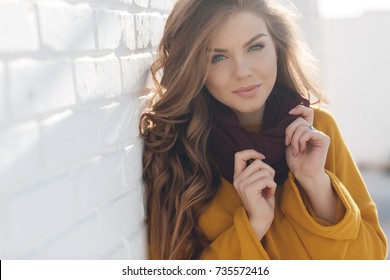 young girl in autumn colors posing near white wall smiling. Autumn woman.  Brown hair and eyes. Warm autumn. Warm spring 