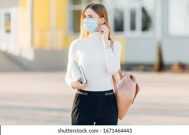 A young girl in the background of a building wears a face mask that protects against the spread of coronavirus disease. Close- up of a young woman with a surgical mask on her face against SARS-cov-2. - Powered by Shutterstock