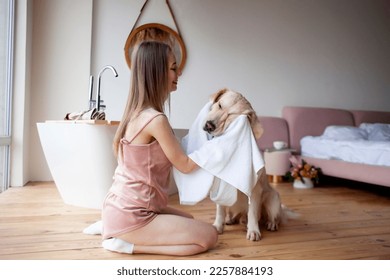 young girl in the bathroom wipes her dog with a towel, a woman dries a golden retriever after bathing - Powered by Shutterstock