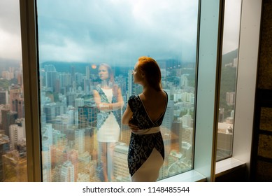 young girl with a beautiful figure , admiring the landscape looking out the window from a high floor, in the afternoon
