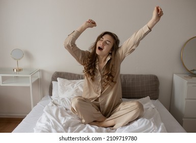 A young girl in beige pajamas is hunched over in bed. The girl yawns in the morning sitting in bed. Selectiv focus