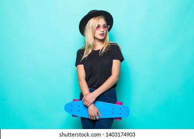 Young Girl In Black Fluffy Hat Holding A Skateboard And Looking At The Camera Isolated On Green Background