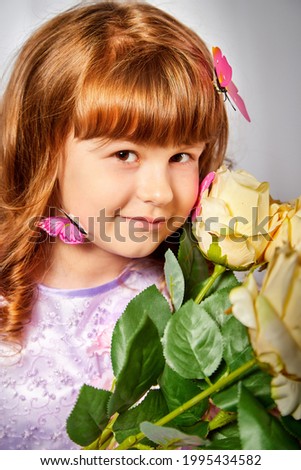 A young girl with blonde curly hair with a butterfly in the studio on a white background. Child posing during a photo shoot. The concept of spring, summer, childhood, happiness