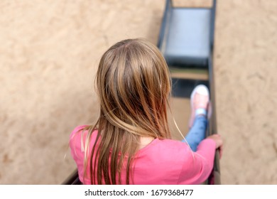 Young Girl With Blonde Hair Sits Alone On A Slide - Selective Focus, Much Copy Space