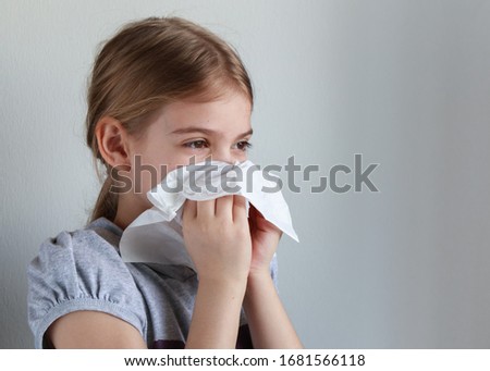 Young girl blowing her nose into a paper handkerchief in front of a white background.