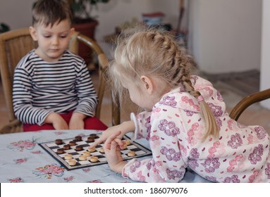 Young Girl And Boy Playing Checkers Or Draughts Together With The Little Girl Bending Over The Board Moving Her Counters Watched Closely By Her Brother