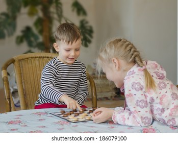 Young Girl And Boy Playing Checkers Or Draughts Together With The Little Girl Bending Over The Board Moving Her Counters Watched Closely By Her Brother