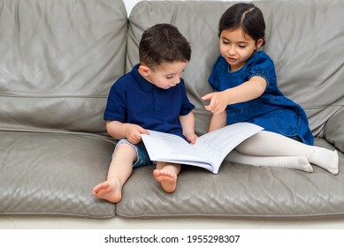 Young Girl And Boy Reading Book Together On Sofa At Home. Family Quality Time Together.