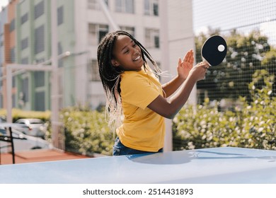 Young girl with braids is concentrating on hitting a ping pong ball with a paddle on a sunny day in an urban environment - Powered by Shutterstock