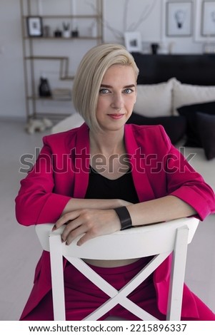 A young girl in a bright pink suit sits on a chair in a bright room. business woman. photo session of a blonde girl. Small business promotion.
