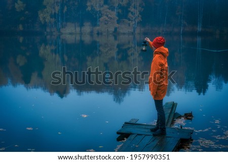 young girl in a bright yellow raincoat with a flashlight is looking for a something in the fog on the lake