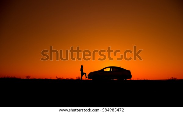 Young girl with and broken
car. Silhouette of sedan car with girl on the background of
beautiful sunset