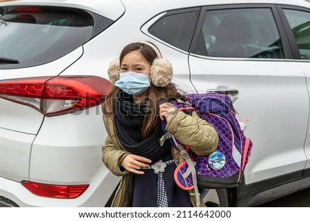 Young girl is brought to school by car.Young girl with satchel on back gets out of car