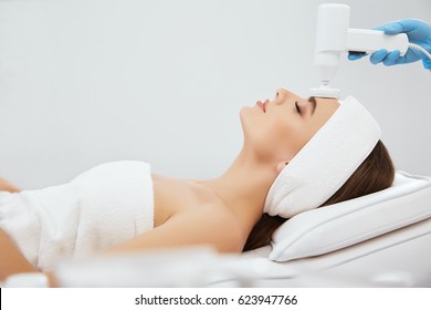 Young Girl With Brown Hair Fixed Behind,clean Fresh Skin Naked Shoulders Wearing White Bath Robe And Hair Bandage, Doing Cosmetic Procedure At Light Medical Background, Brushing.